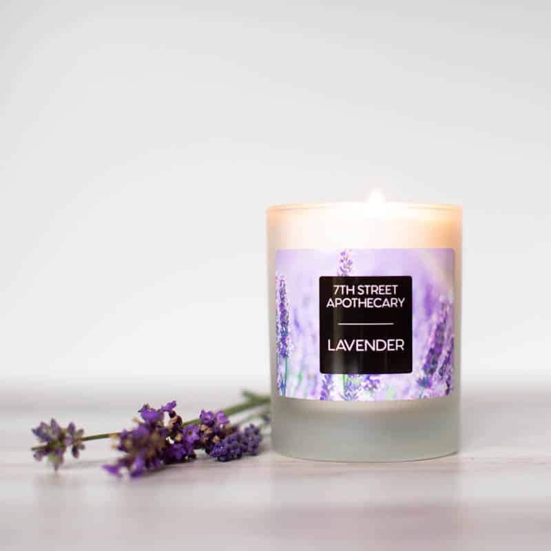 Custom Lavender Label for Homemade and Small Batch Candles. Shows a photo of a candle and lavender flowers. The candle has a label with lavender flowers in the background, with a centered black box with white text reading "7th Street Apothecary - Lavender"