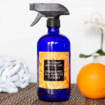 Homemade Orange Peel Cleaner in a blue bottle with a glossy orange personalized label