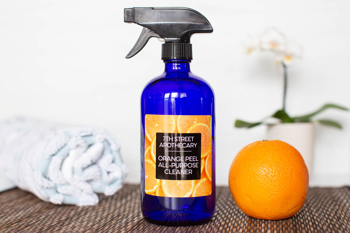 Homemade Orange Peel Cleaner in a blue bottle with a glossy orange personalized label